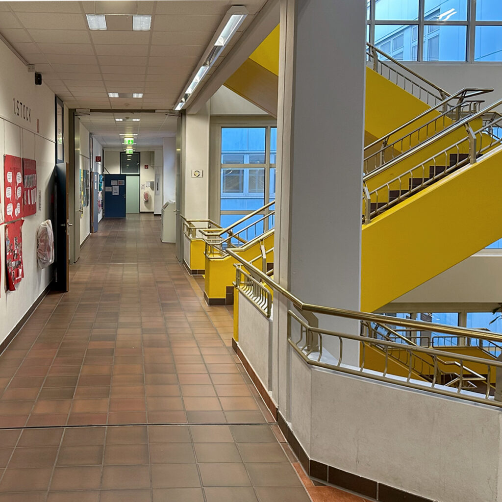 Gang im Schulgebäude, rechts das gelbe Stiegenhaus